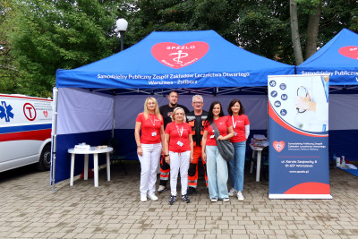 Na tle stoiska SPZZLO Warszawa Żoliborz-Bielany grupa pracowników biorących udział w pikniku pn. Kosmiczne urodziny Placu Wilsona.
