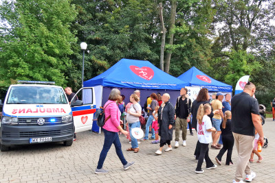 Na tle głównym stoisko SPZZLO Warszawa Żoliborz-Bielany z pacjentami ustawionymi w kolejce.