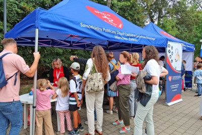 Stoisko SPZZLO Warszawa Żoliborz-Bielany z pacjentami ustawionymi w kolejce, widok boczny.