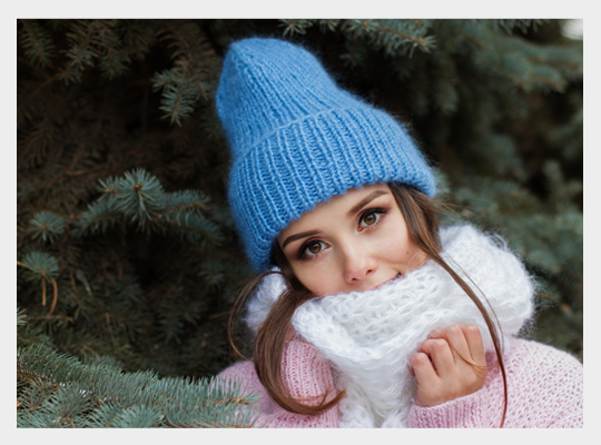 Dziewczyna stoi obok zaśnieżonego drzewa z czapce i szaliku