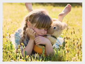 Dziewczynka leżąca na trawie przytula misia